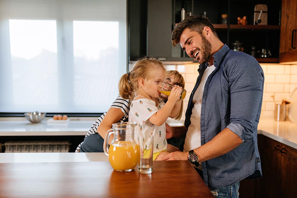 An adorable little girl and her parents drinking juice together at home