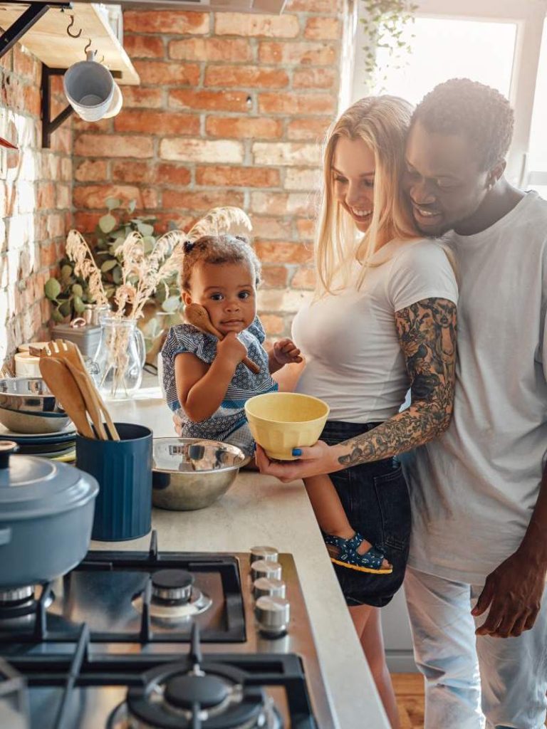 Shot of young mixed race family cooking food together on cozy kitchen in daytime.